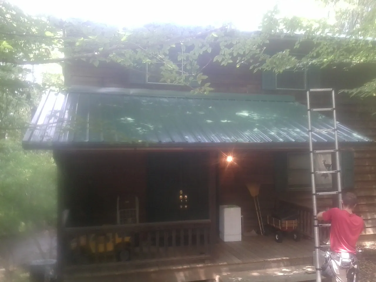 Worker on a ladder at the green porch roof of a wooded cabin in Atwater